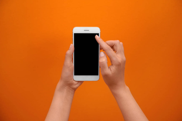Young woman holding mobile phone with blank screen in hand on color background - Fotó, kép