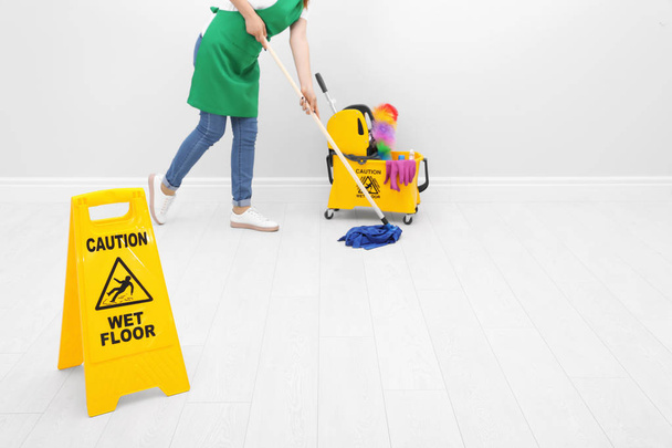 Safety sign with phrase "CAUTION WET FLOOR" and young woman cleaning, indoors - Photo, Image