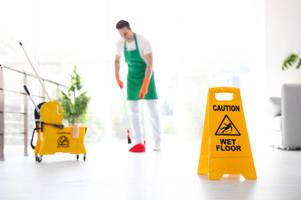 Safety sign with phrase "CAUTION WET FLOOR" and young man on background - Foto, imagen