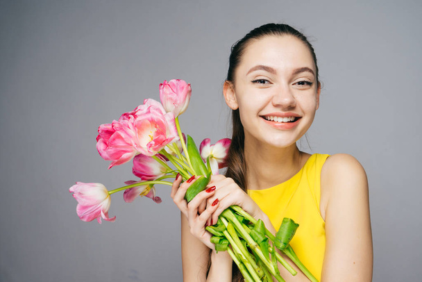 happy smiling girl in yellow dress is holding in hands a fragrant pink flowers, smiling - Photo, Image