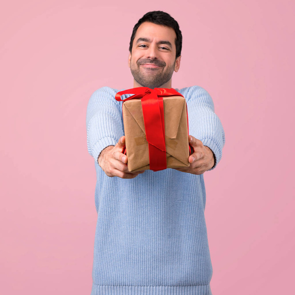 Man met blauwe trui holding geschenkdozen in handen op roze achtergrond - Foto, afbeelding