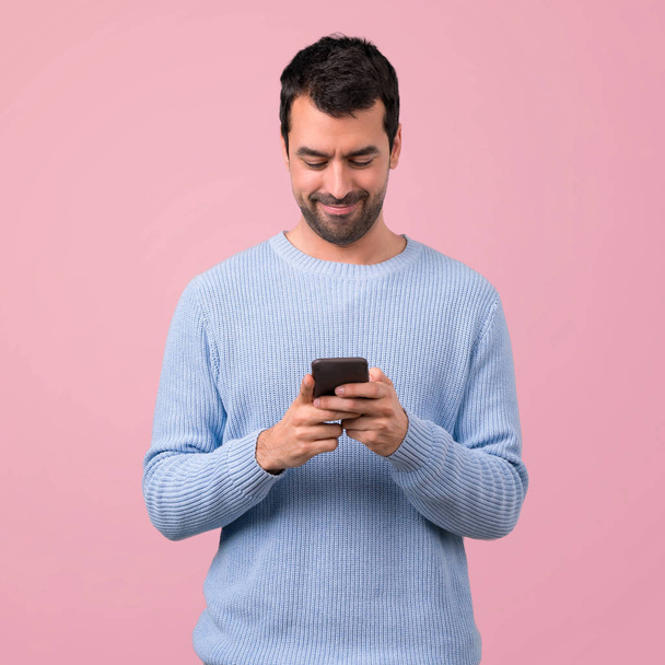 Man met blauwe trui met behulp van mobiele telefoon op roze achtergrond - Foto, afbeelding