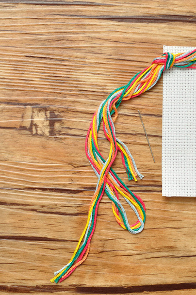 Corda de fio de bordado colorido exibido com um pedaço de tecido de bordado e uma agulha
 - Foto, Imagem