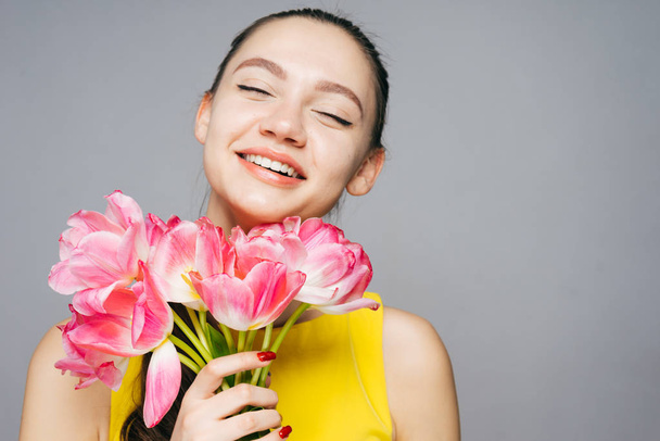 joyful beautiful girl in a yellow dress laughs, enjoys the spring and keeps flowers - Фото, изображение