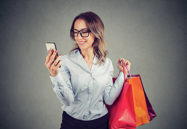 Piękna kobieta, zakupy online sprawdzanie cen na telefon komórkowy. Moda dziewczyna z kolorowe torby patrząc na telefon. - Zdjęcie, obraz