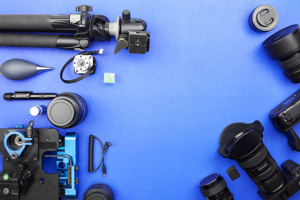 Ψηφιακή κάμερα με φακούς και εξοπλισμό του επαγγελματία φωτογράφου σε μπλε φόντο χαρτιού - Φωτογραφία, εικόνα