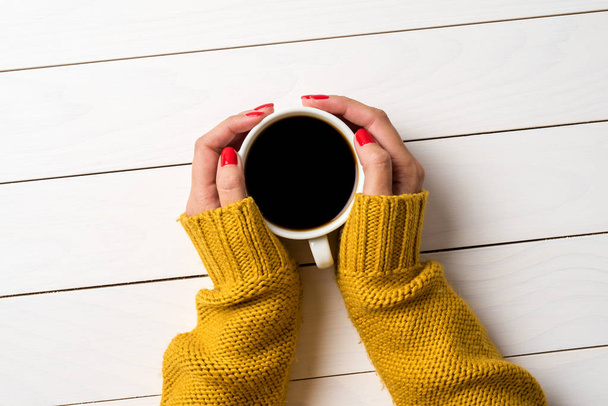 Γυναικεία χέρια στο ζεστό πουλόβερ κρατώντας το φλιτζάνι του καφέ - Φωτογραφία, εικόνα