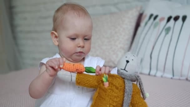 A beautiful little girl is playing with a soft toy rabbit on the bed. - Materiał filmowy, wideo