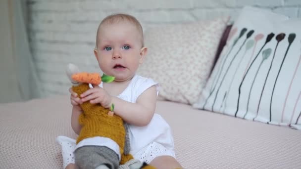 A beautiful little girl is playing with a soft toy rabbit on the bed. - Felvétel, videó