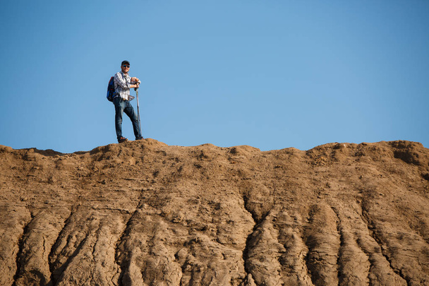 Image of afar of tourist man with sticks for walking on hill against blue sky - Zdjęcie, obraz