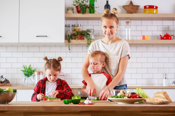 Imagem de mãe com filha e filho cozinhando à mesa
 - Foto, Imagem