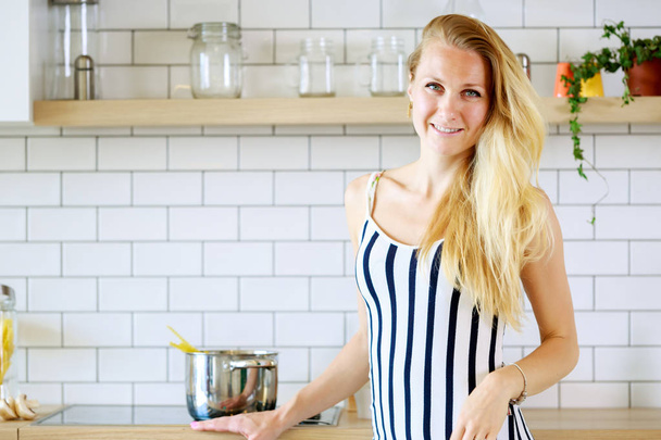Portrait of beautiful woman in long striped dress in kitchen - Fotó, kép