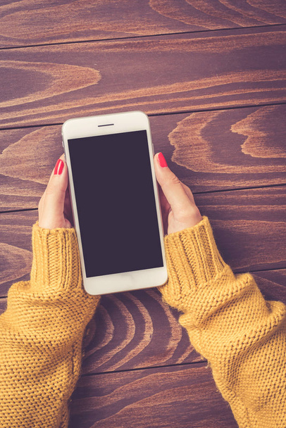 Female hands in warm sweater holding white smart phone. Close up - Foto, immagini