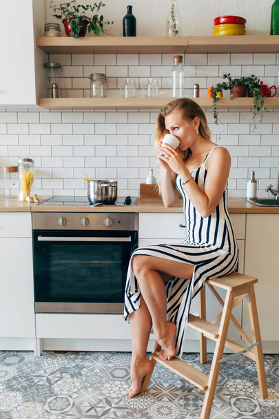 Photo of beautiful woman in long striped dress in kitchen - Foto, imagen