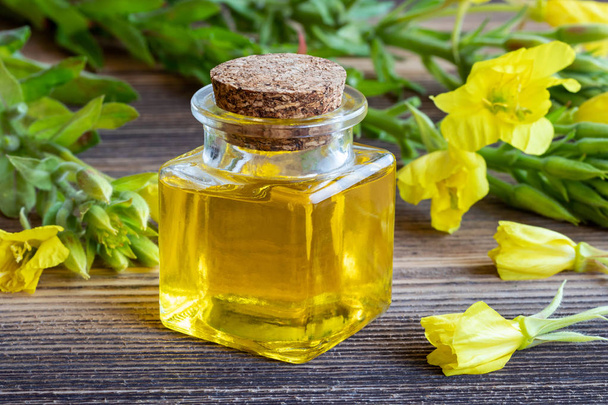 Láhev pupalkový olej a čerstvé kvetoucí rostliny na dřevěné pozadí - Fotografie, Obrázek