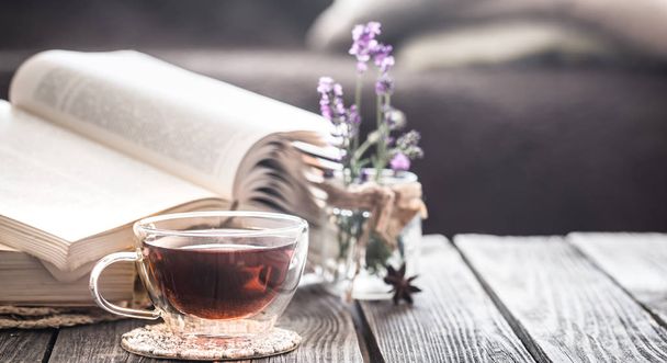 cup of tea with a book in the interior with lavender flowers in a transparent vase on a wooden background - Foto, Bild