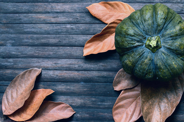 Green pumpkin and yellow leaves moody toned photo. Autumn harvest banner template. Dry leaf and squash ornament on wooden table. Rustic flat lay with dry leaf decor. Fall seasonal top view photo - Foto, imagen