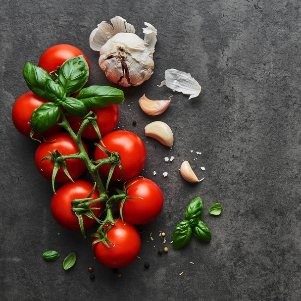 Food background. Flat lay of fresh tomatoes with basil, garlic and seasalt on black stone background. Square crop, top view. - Photo, image
