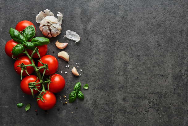 Food background. Flat lay of fresh tomatoes with basil, garlic and seasalt on black stone background. Top view with copy space on the right. - Photo, image