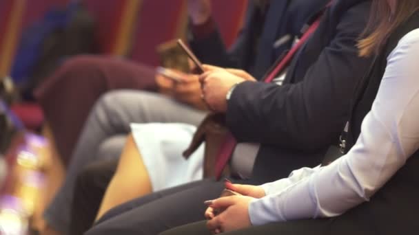 Pessoas sentadas em conferência de negócios, homem com smartphone nas mãos
 - Filmagem, Vídeo