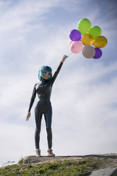 cool leuk persoon in de pop gezicht masker en latex rubber fetish kostuum genieten van het leven op de blauwe hemelachtergrond - Foto, afbeelding
