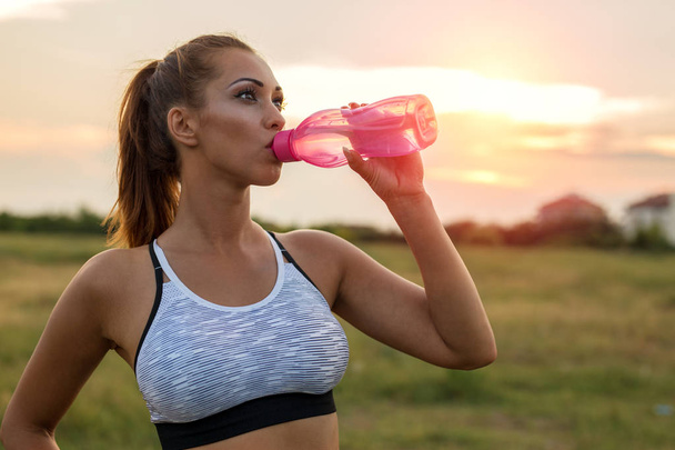 Belle jeune femme buvant de l'eau à l'extérieur pendant l'entraînement au coucher du soleil
 - Photo, image