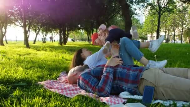 Happy family lies on the grass and plays with the child at sunset in the park - Кадры, видео