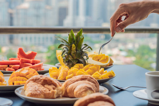 Сніданок з кавовими фруктами та хлібом на балконі на тлі великого міста
. - Фото, зображення