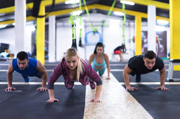 groep jonge gezonde mensen doen pushups op grensoverschrijdende fitness gym - Foto, afbeelding