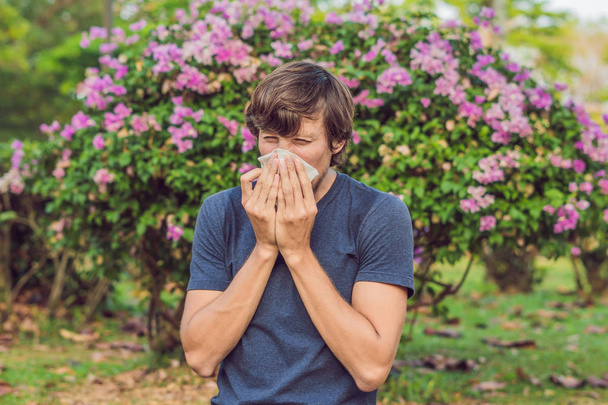 Young man sneeze in park against background of a flowering trees. Allergy to pollen concept. - Fotoğraf, Görsel
