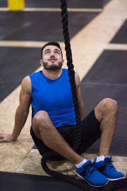 young muscular man sitting and relaxing before rope climbing in cross fitness gym - Foto, immagini