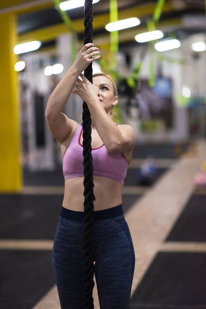 young muscular woman doing rope climbing in cross fitness gym - 写真・画像
