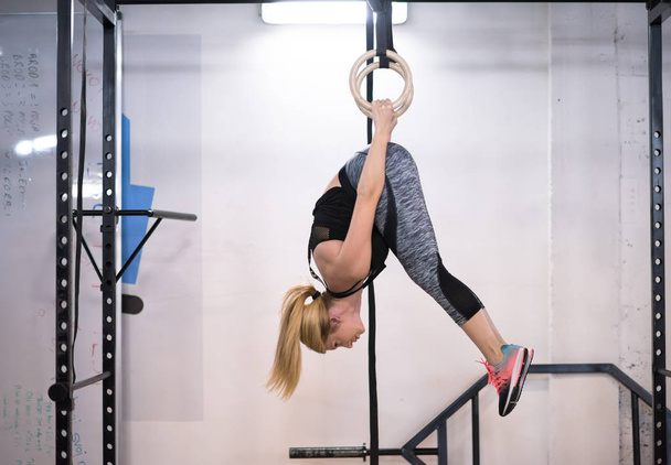 young athletic woman working out on gymnastic rings at the cross fitness gym - Фото, изображение
