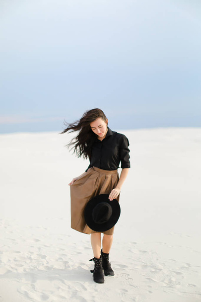 Καυκάσιος γυναίκα φωτογραφία μοντέλο φοράει φούστα, μαύρη μπλούζα με καπέλο και στέκεται στο χιόνι. - Φωτογραφία, εικόνα