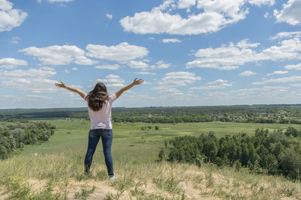 Молода дівчина-хіпстер подорожує у літні канікули. Жінка в сучасному одязі стоїть на пагорбі і дивиться на поле. Синє небо і білі хмари. Концепція свободи та способу життя. Прекрасна природа
 - Фото, зображення