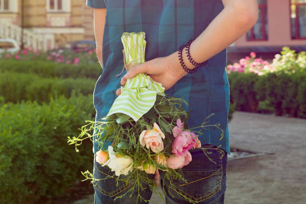 Teenager boy holding bouquet of flowers behind his back. Surprise, gift, present. - Φωτογραφία, εικόνα