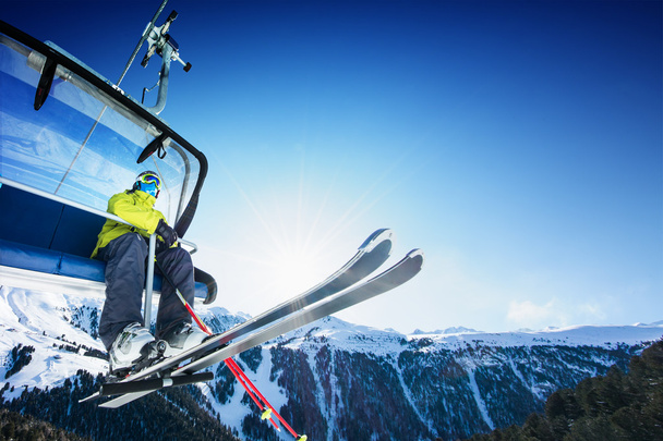 Hiihtäjä istuu hiihtohississä - hissi aurinkoisena päivänä ja vuori
 - Valokuva, kuva