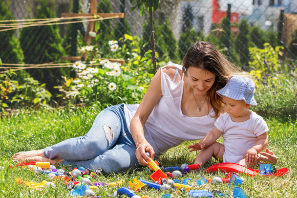 Young mother with her toddler child, boy, playing in garden with colorful construction - 写真・画像