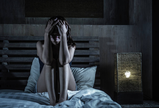 young sad and depressed woman sitting on bed thoughtful and worried about problem or feeling sick and unwell covering face with hands in stress and depression feeling frustrated in pain - Foto, Imagem