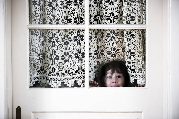 Little preschool boy, child, looking out scared through a door with windows - Foto, Imagem
