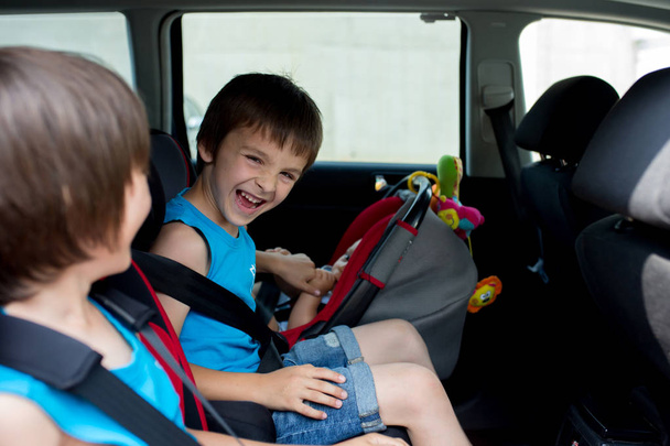 Маленький мальчик и его старшие братья, путешествуя на автомобильных сидениях, отправляясь в отпуск, путешествуя на заднем сидении
 - Фото, изображение
