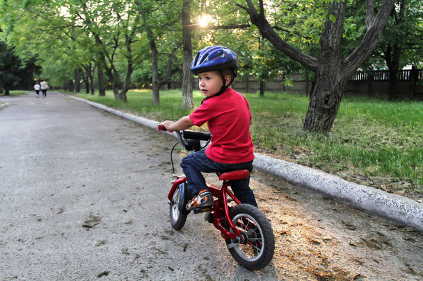 Um rapazinho branco, com um capacete protector na cabeça, anda de bicicleta. Criança em uma bicicleta vermelha de duas rodas
. - Foto, Imagem