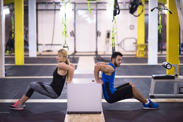 young couple athletes working out their arms using boxes at cross fitness gym - Photo, image