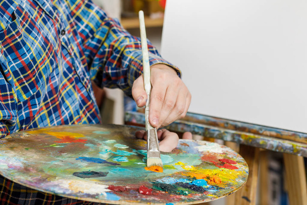 de hand van een man met een penseel op het doek. kunst, creativiteit, hobby en mensen - Foto, afbeelding