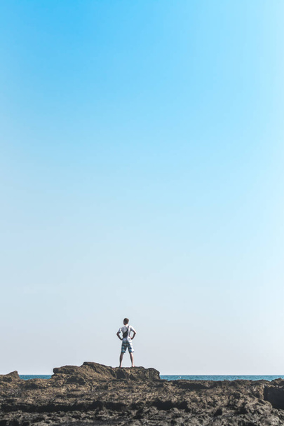 男は海のバリ島の岩の上に立っています。インドネシア. - 写真・画像