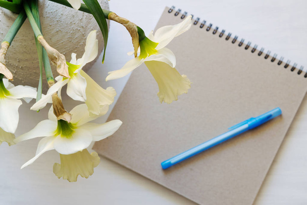 Notepad with pen, daffodils in a vase on a white table. - Фото, зображення