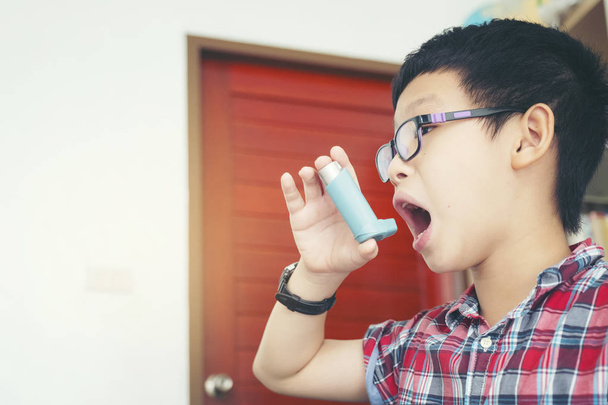 niño con spray, niño usando su inhalador de bomba de asma en casa, concepto de alergia
 - Foto, imagen