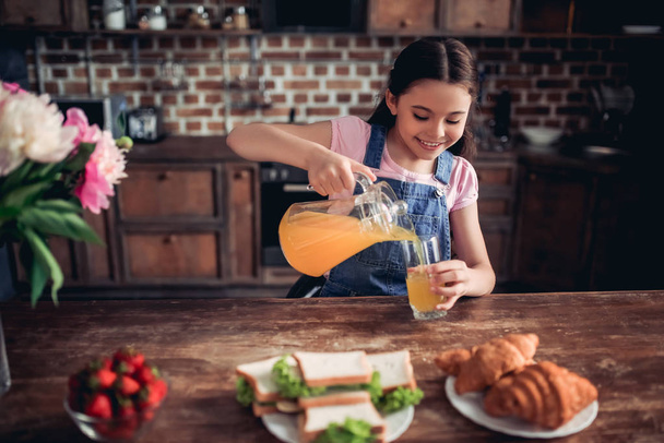 portrait of smiling girl pouring ornge juice into the glass for breakfast at the kitchen - Foto, Bild
