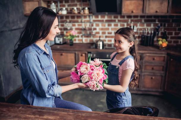 small daughter giving a bouquet of peonies to her mother at the kitchen - 写真・画像