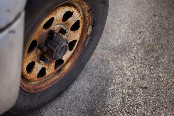 A closeup view of a heavily used car tyre that seems abandoned a longtime ago. There are also rusted rim hubcap and  screws that badly needs maintenance. - Photo, Image